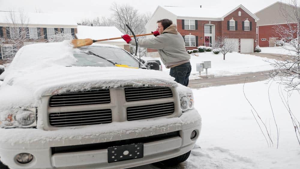 A man is cleaning snow with brush form top of his car