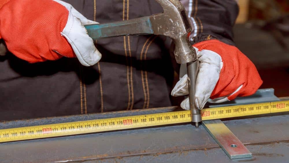 A man punches metal with a hammer and center punch