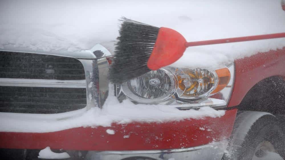 A man is cleaning snow with brush from his car headlight