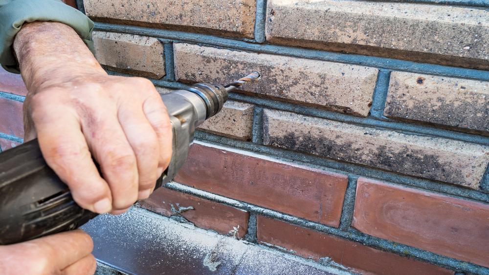 old man drills outdoor brick wall
